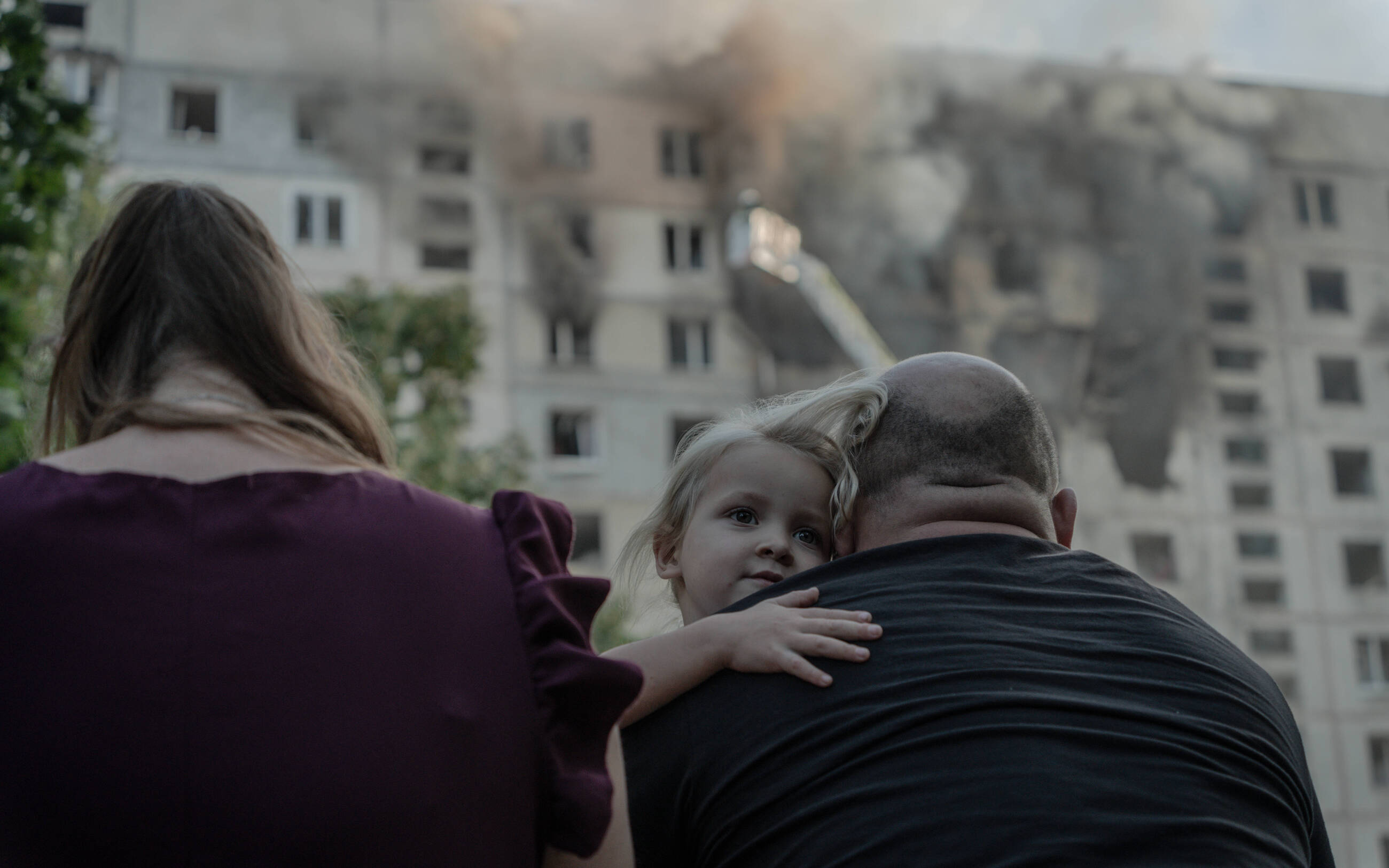 A girl hugging her parents in front of the burning high-rise in Kharkiv, after it was hit by a glide bomb. September 15, 2024 / Photo: Ivan Samoilov, Gwara Media