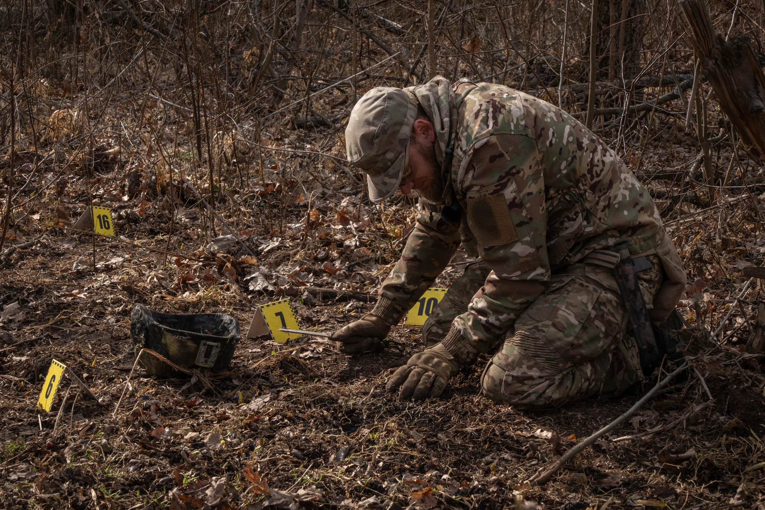 Volunteer Oleksii Yukov puts number signs for evidence around the body of a fallen Russian soldier in Donetsk region, March 2025.