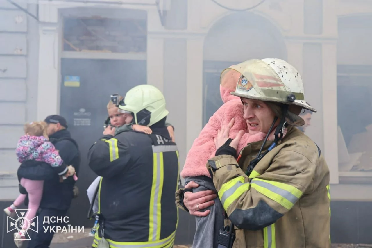 Emergency workers holding children after Russian drone strike on the kindergarten.