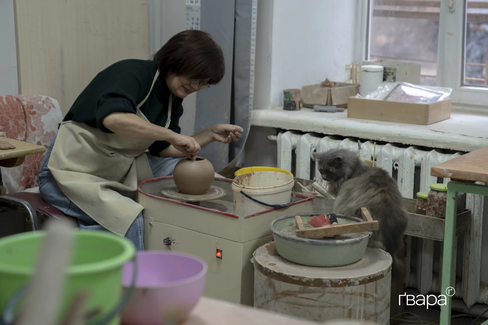 Наталія Широка за роботою над глиняним чайником, поруч кішка Роксі