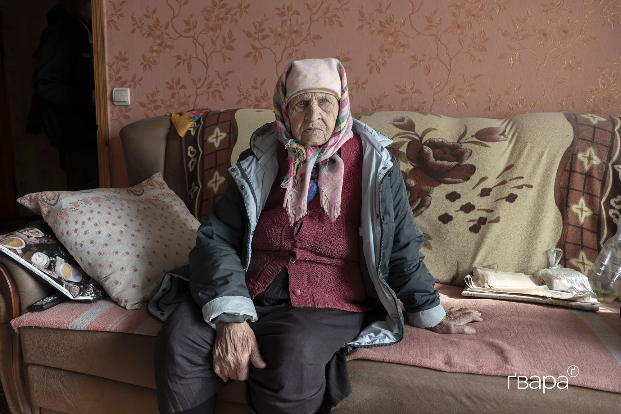 88-річна Марія сидить на дивані своєї розбитої квартири