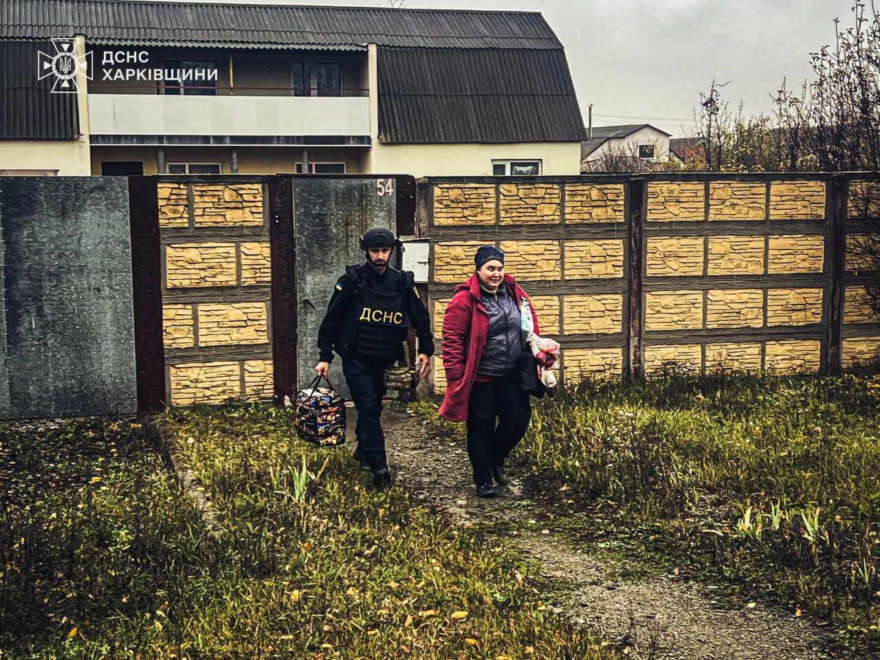 A woman walks with a rescuer to a car to evacuate with her child from Velykyi Burluk due to Russian attacks