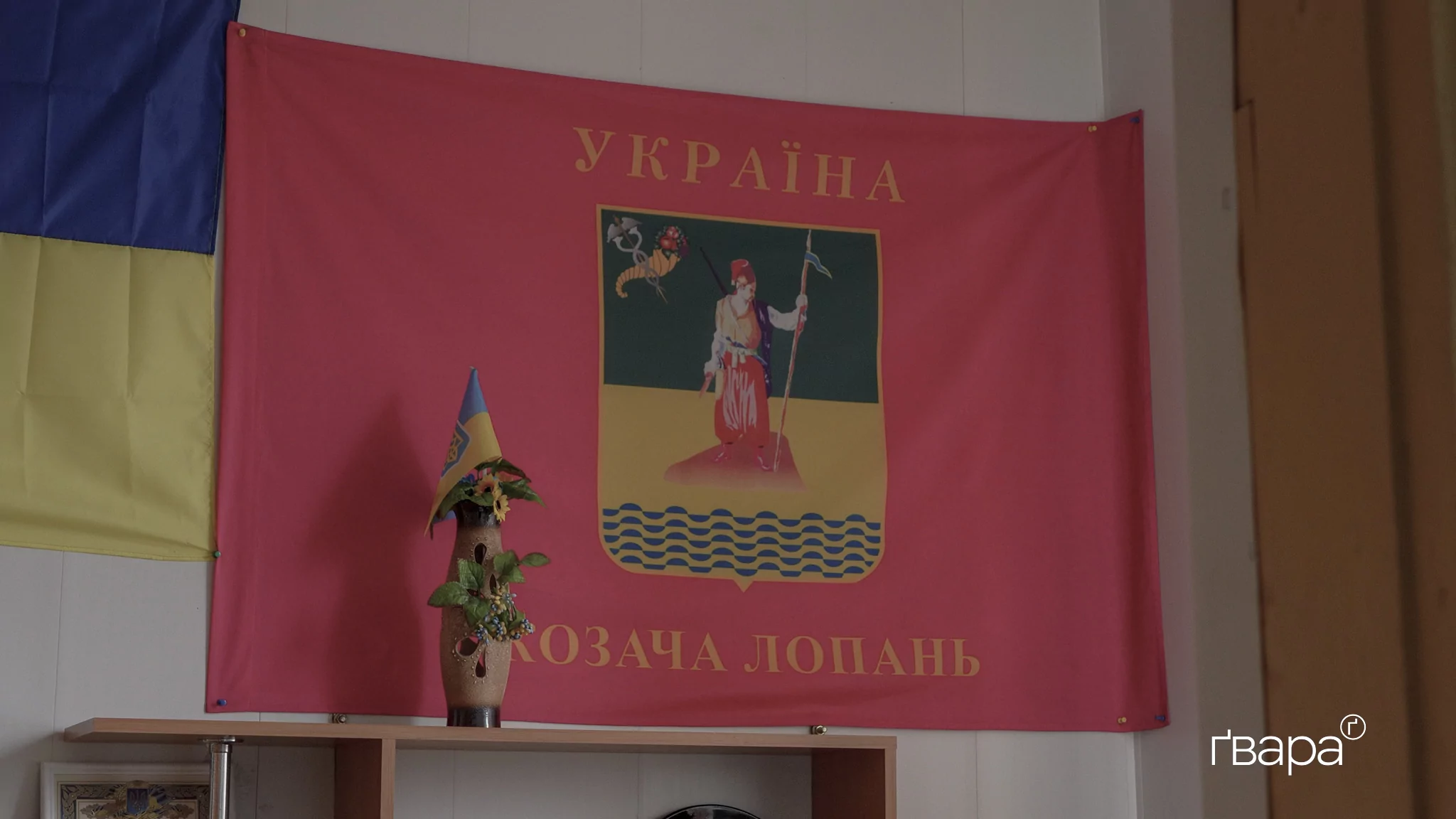 Червоний прапор з зелено-жовтим зображенням у середині з надписами «Україна» і «Козача Лопань»