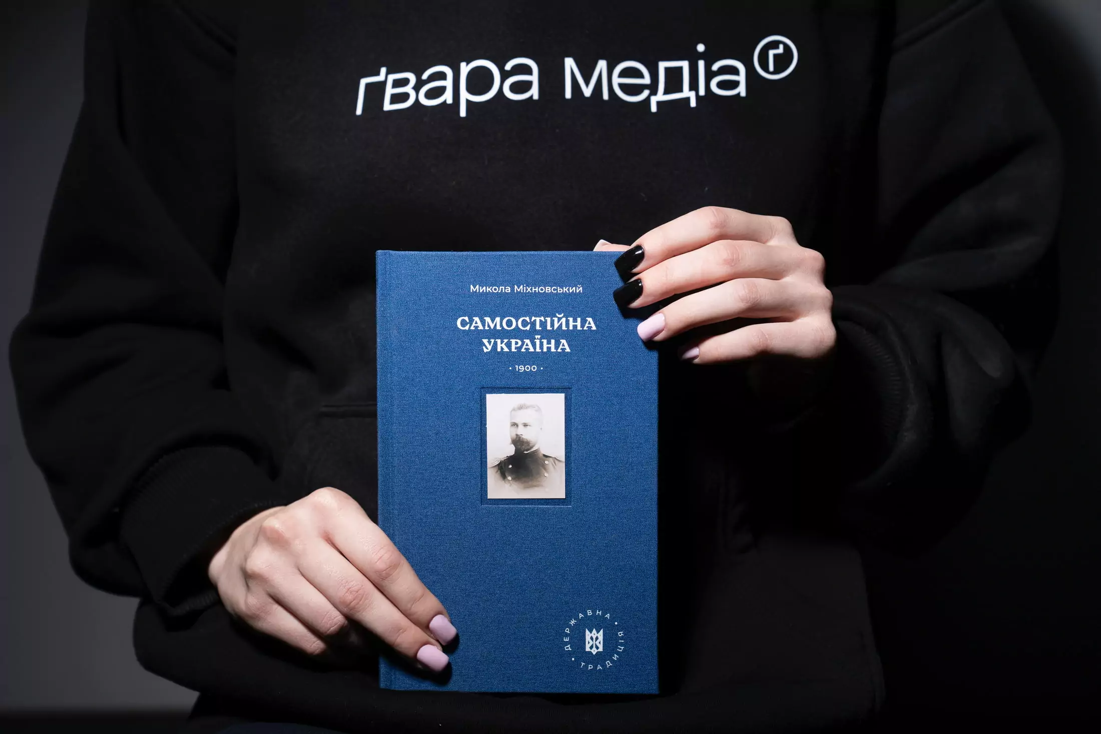 Книжка «Самостійна Україна» Миколи Міхновського у руках у людини в худі з надписом Ґвара Медіа