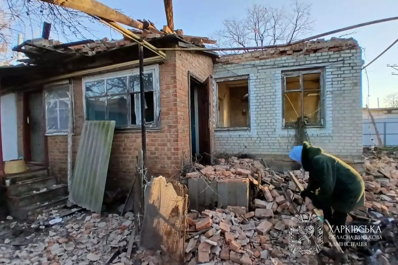 House damaged by Russian shelling, a figure of a local picking up debris in front of it