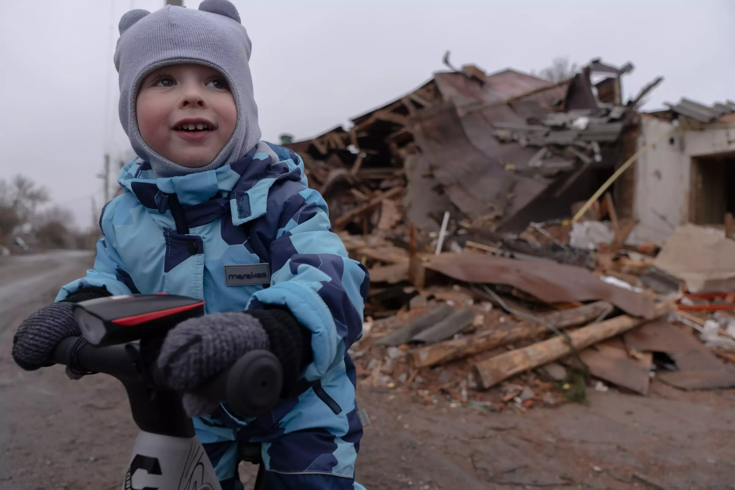 A child is playing in front of a destroyed residential building in the background. Russian troops hit that building with a glide bomb. Zolochiv, January 2025