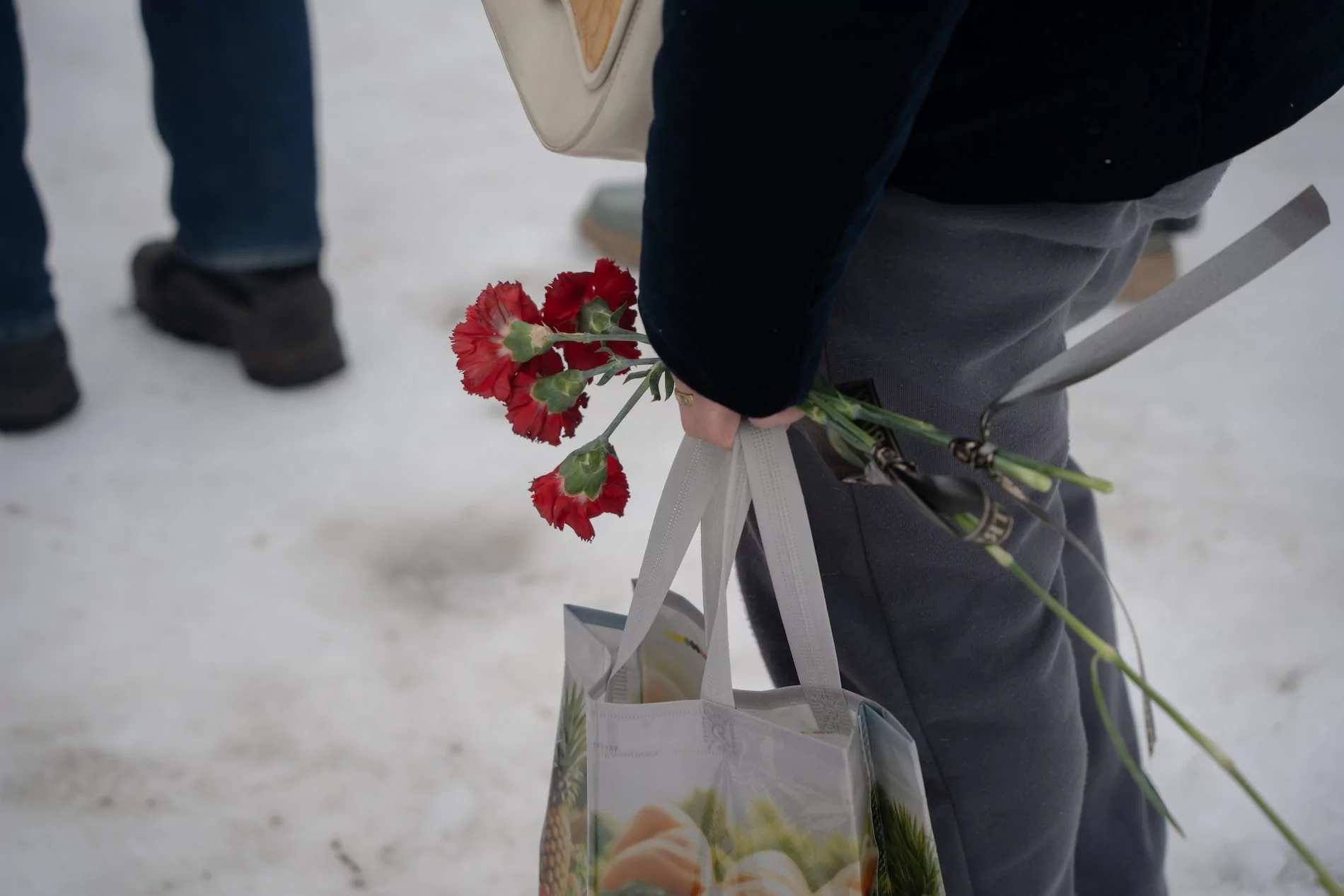 A person holding red flowers and a tote bag