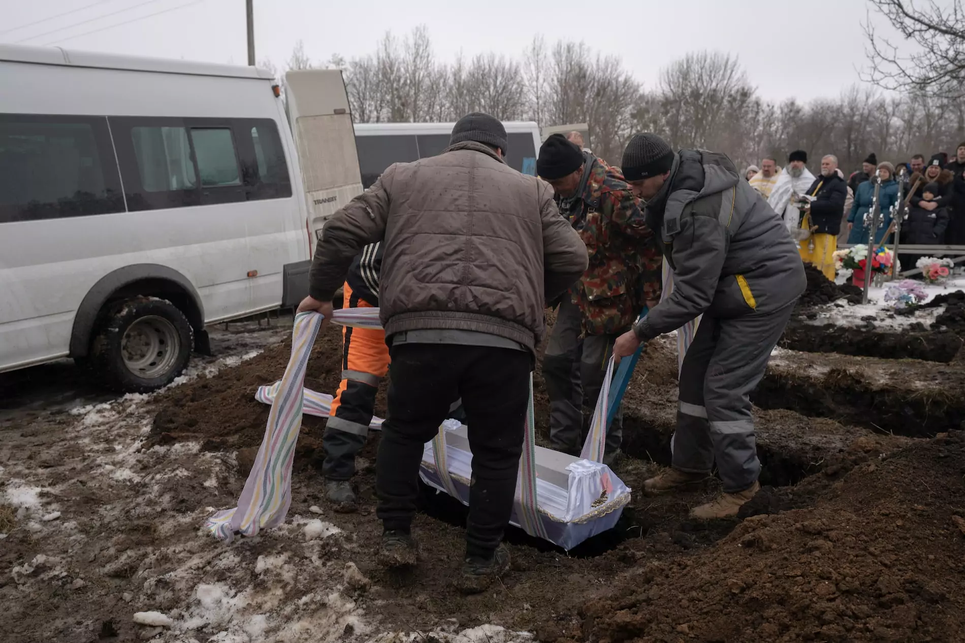 Cemetery workers are putting down small white coffin into the earth