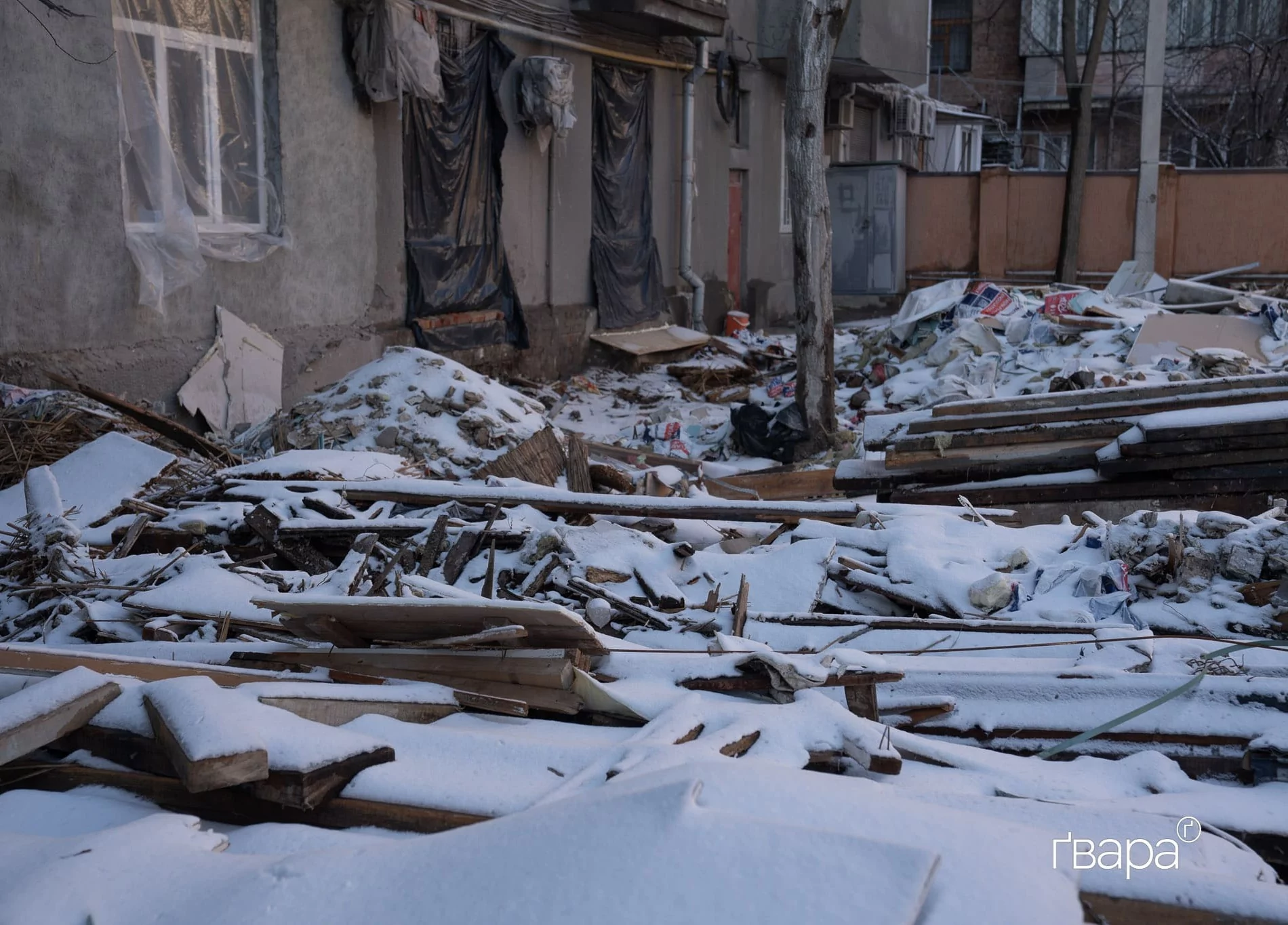 Вкриті снігом будівельні матеріали перед будинком