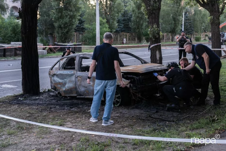 Чоловіки, що стоять поряд з машиною, яка згоріла після російського удару «бандероллю»