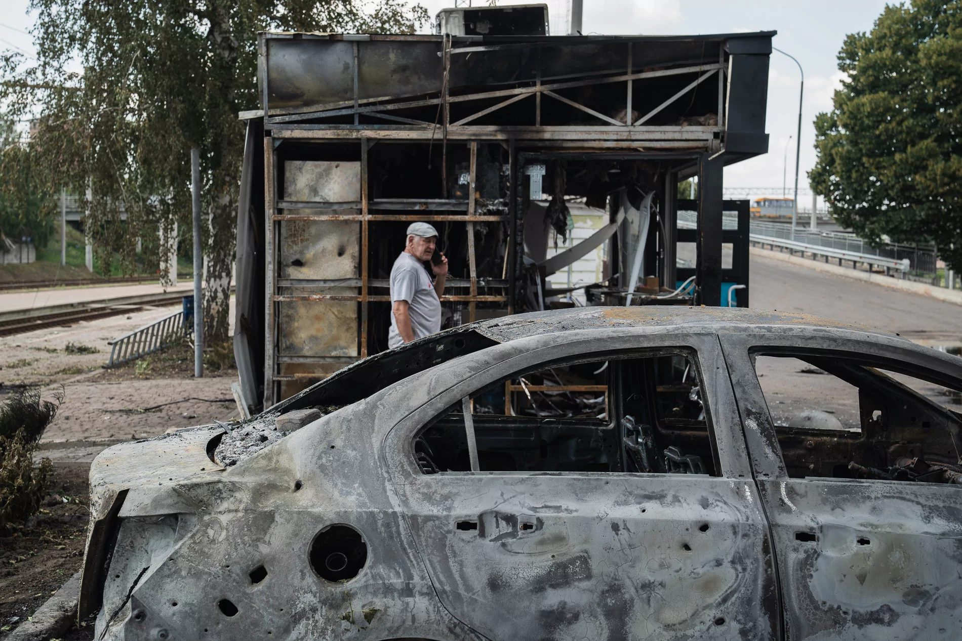 A man is standing near destroyed car and a kiosk at the railway station